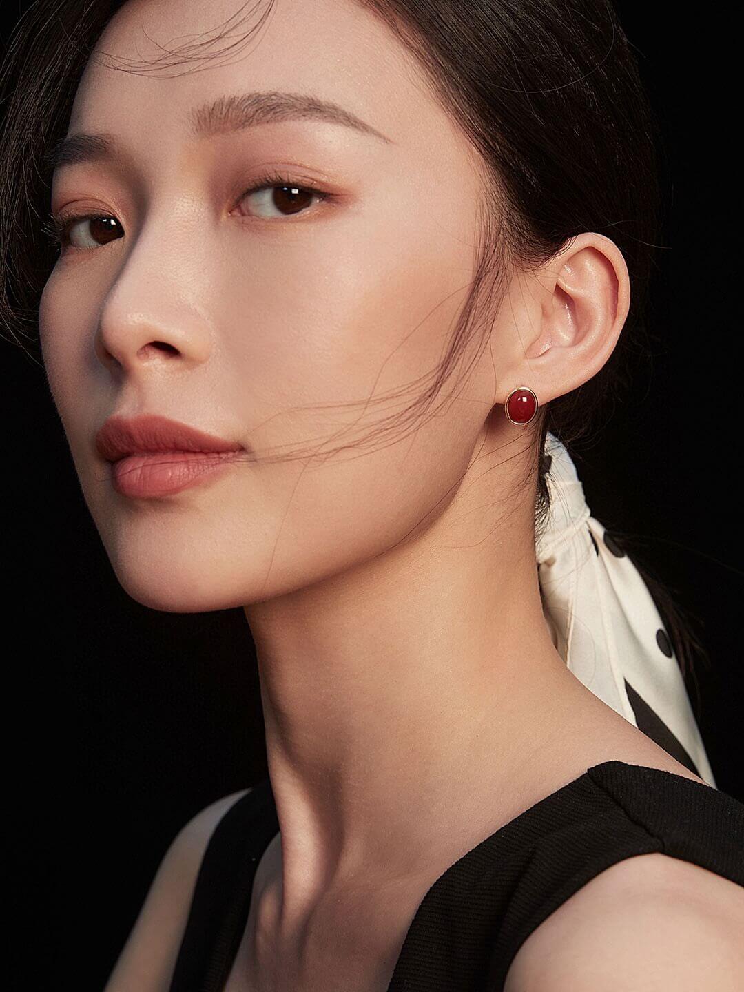 Close-up of a woman wearing a red earring against a dark background