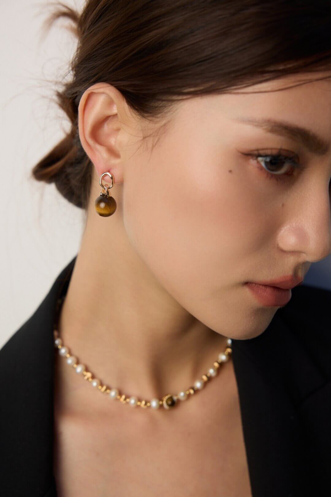 Close-up of a person wearing a pearl necklace and earrings with a neutral background