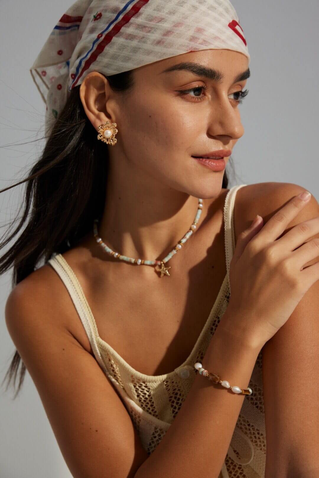 Woman wearing a headscarf, tank top, and jewelry against a neutral background