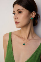 Woman wearing green earrings and a necklace against a plain background