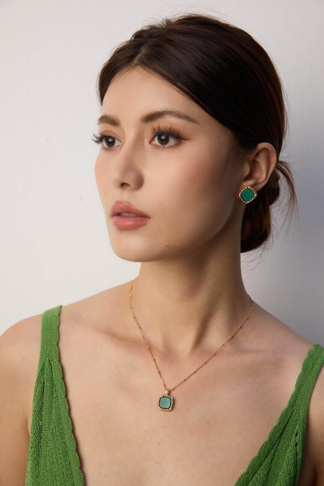 Woman wearing green earrings and a necklace against a plain background