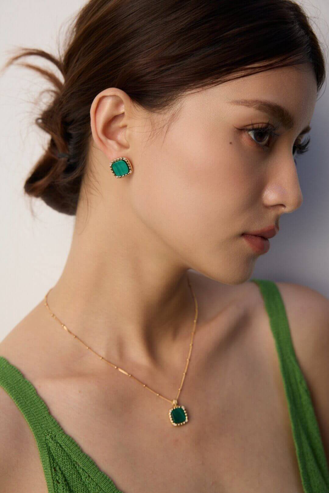 Woman wearing green gemstone earrings and necklace against a neutral background