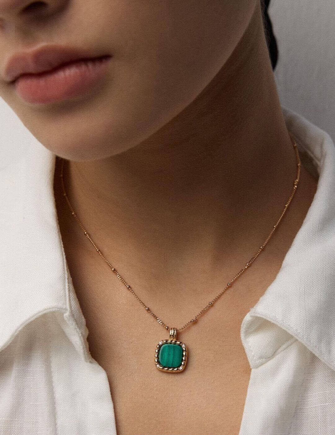 Necklace with a green pendant worn by a person in a white shirt.