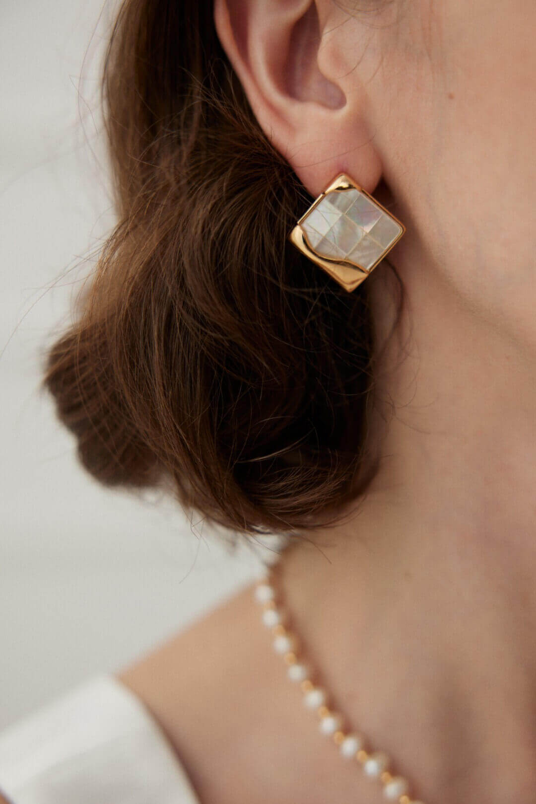 Side view of mosaic shell earrings on model, showcasing unique geometric design against skin.