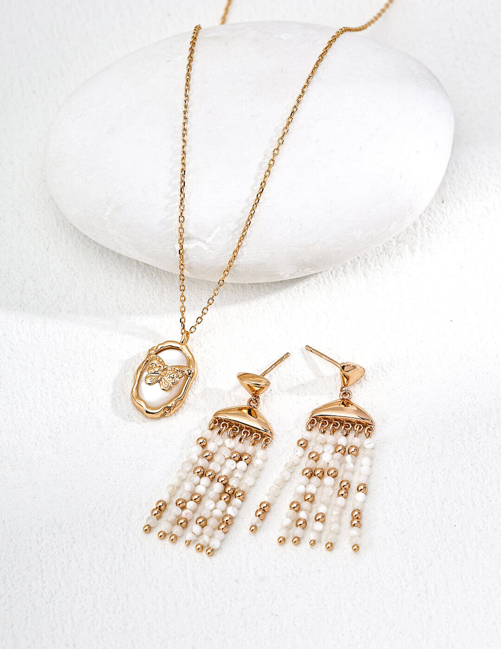 Gold necklace and earrings with pearl details on a white background