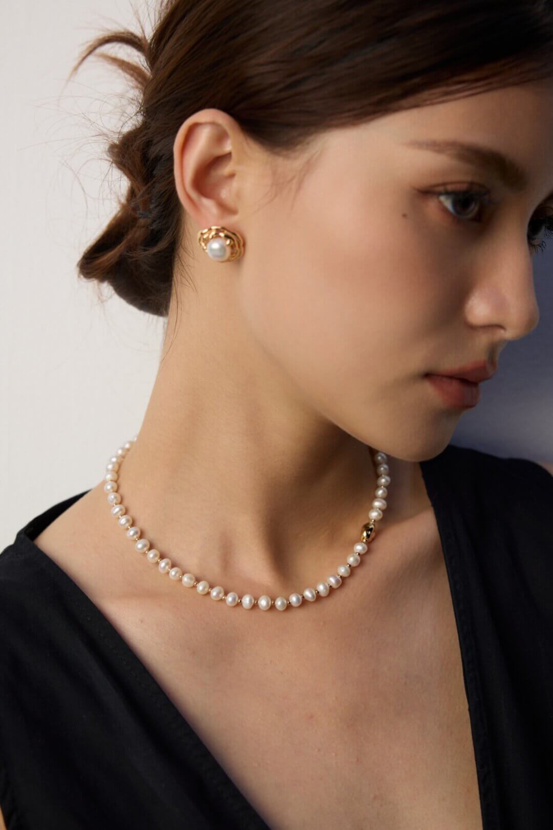Woman wearing a pearl necklace and earring against a neutral background