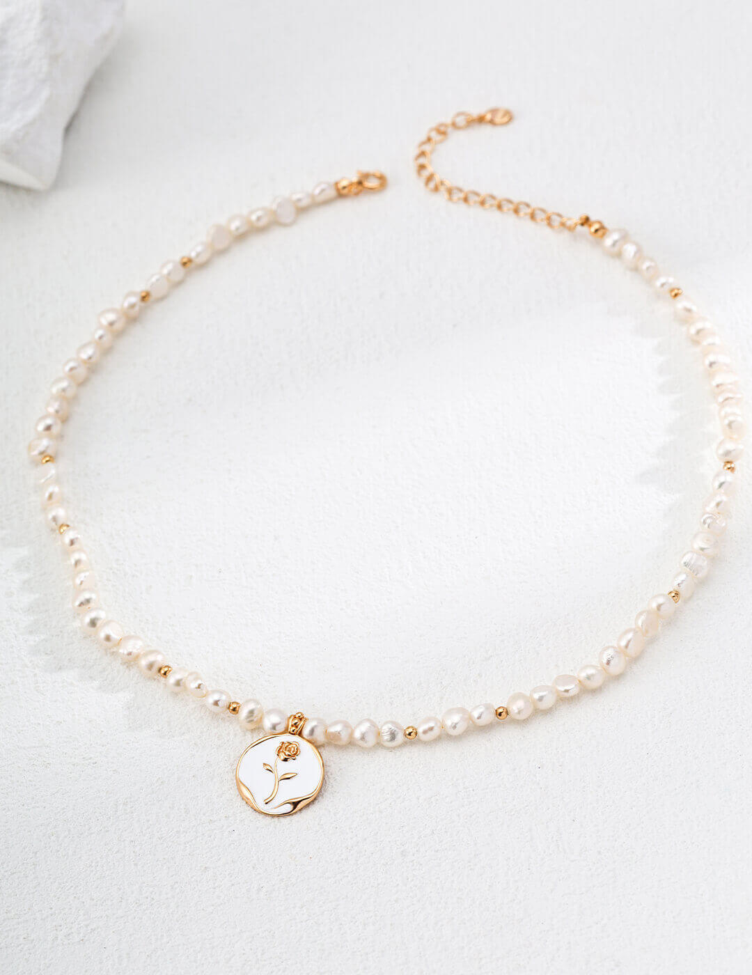 Natural pearl and enamel rose necklace in sunlight, highlighting the pearl's glow and rose's vibrant color.
