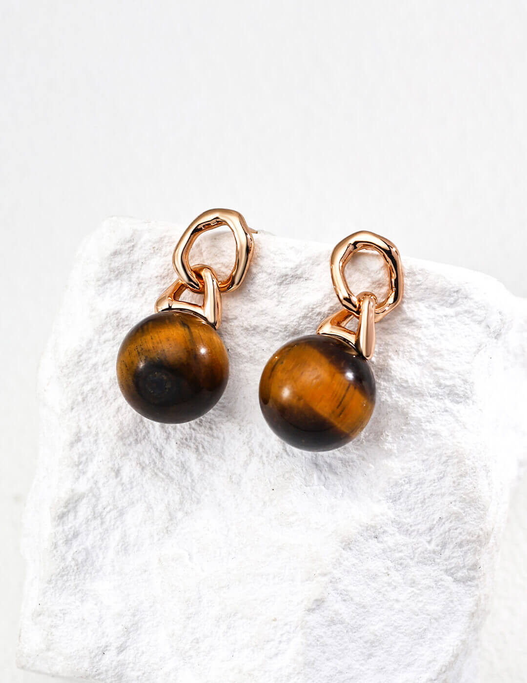 Tiger eye stone earrings with rose gold hooks on a textured white surface