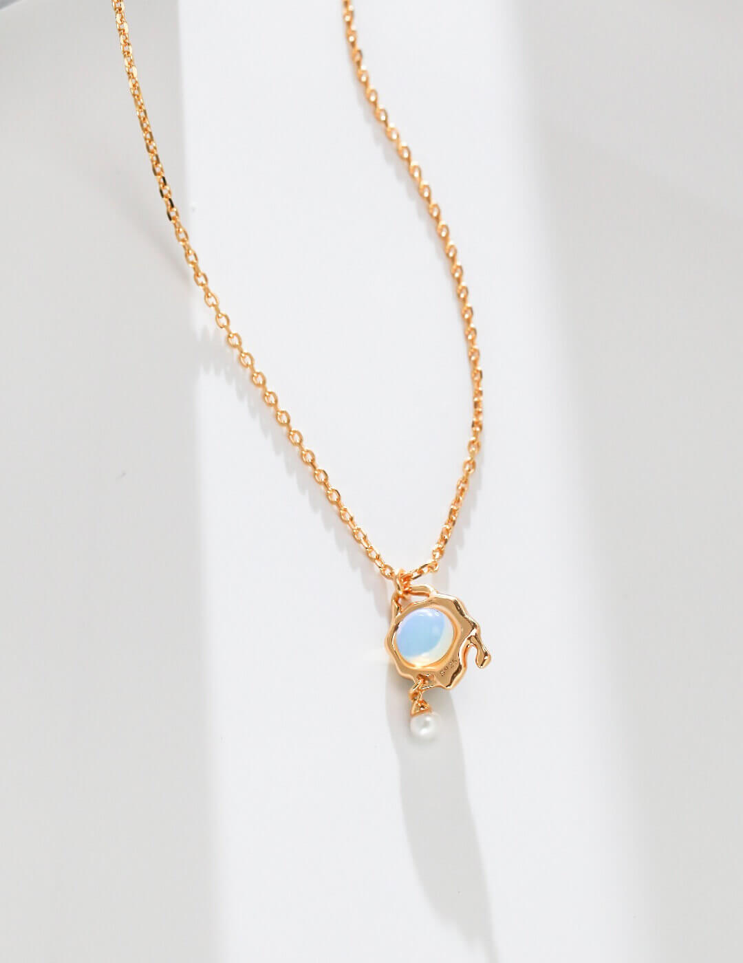 Gold necklace with a blue gemstone and pearl on a white background