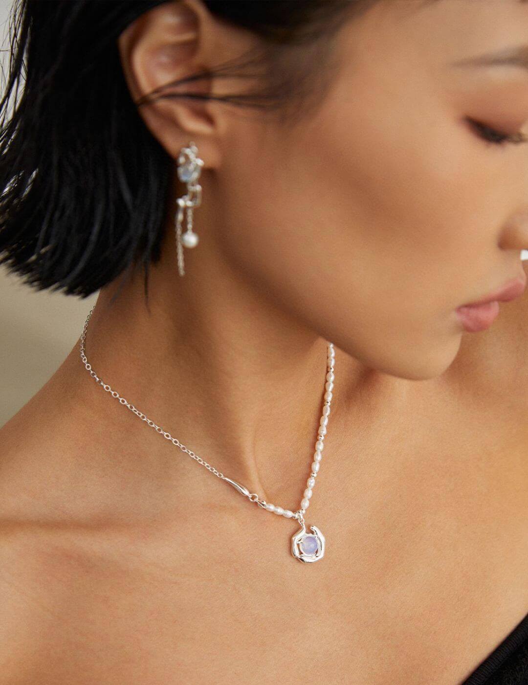 Opal and pearl necklace resting on model's neck, showcasing the fluid silver mountain and blue opal lake design.