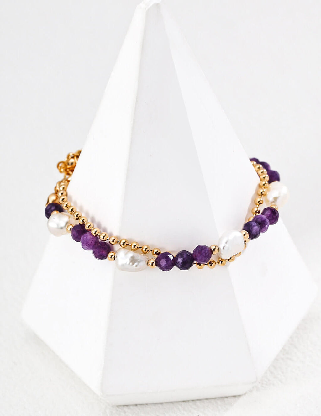 Necklace with purple beads and gold chain on a white stand