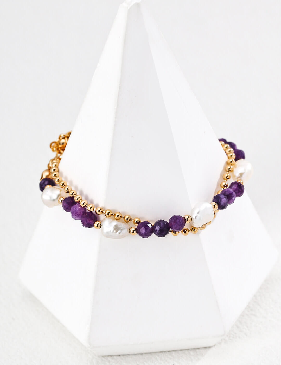 Necklace with purple beads and gold chain on a white stand