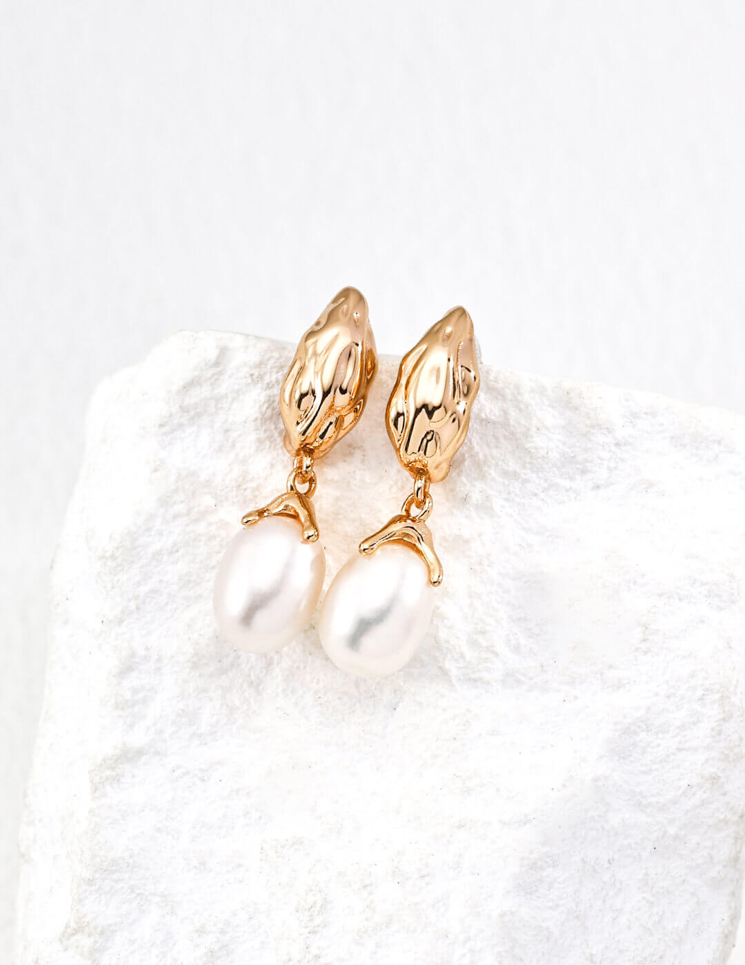 Gold earrings on a white textured surface
