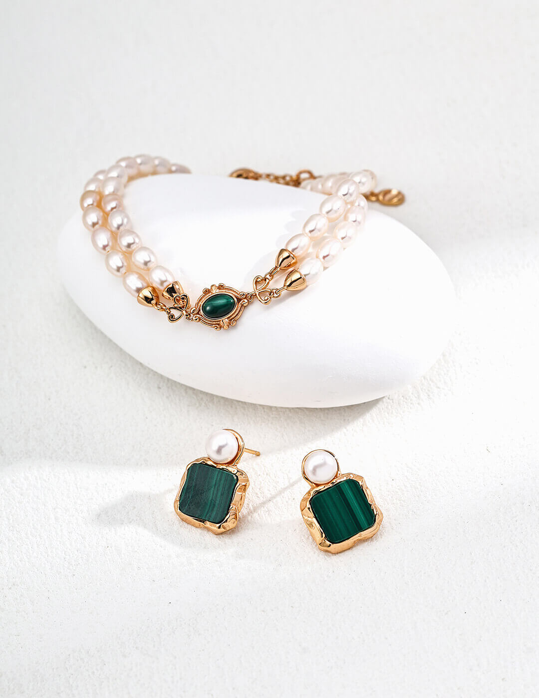 Jewelry set with green gemstone earrings and gold bracelet on a white background