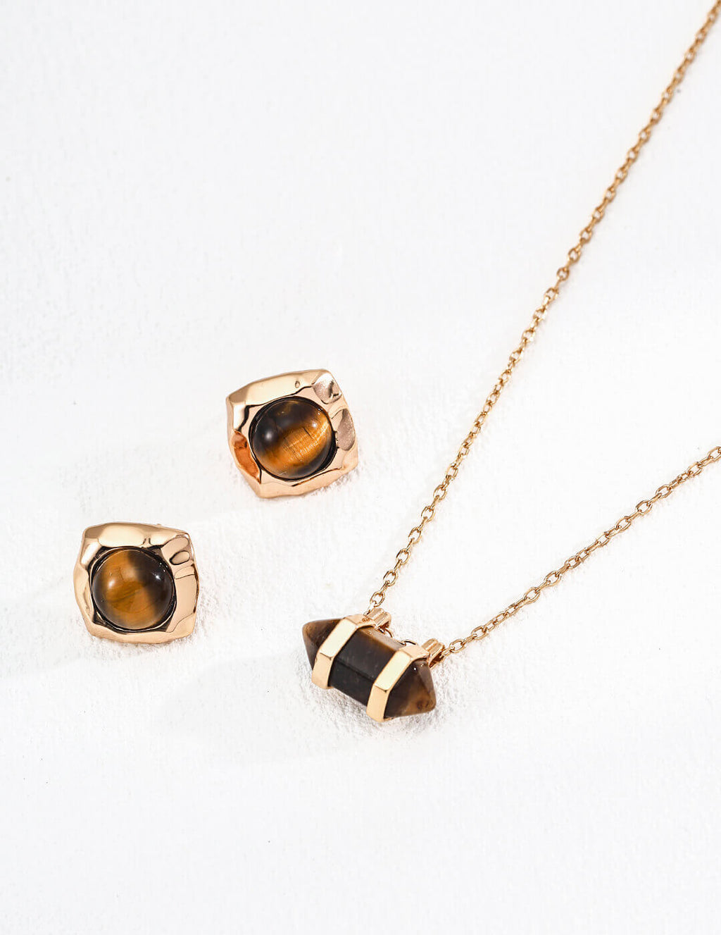 Gold necklace and earrings with tiger's eye stones on a white background