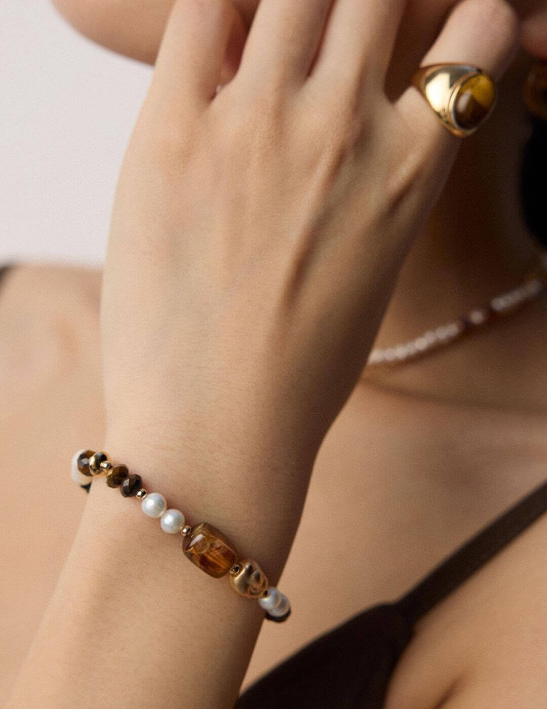 Hand wearing a bracelet with gold and pearl beads on a neutral background