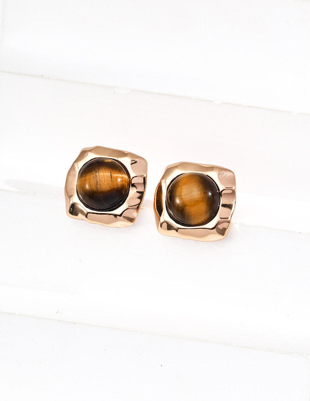 Pair of gold earrings with tiger's eye stones on a white background
