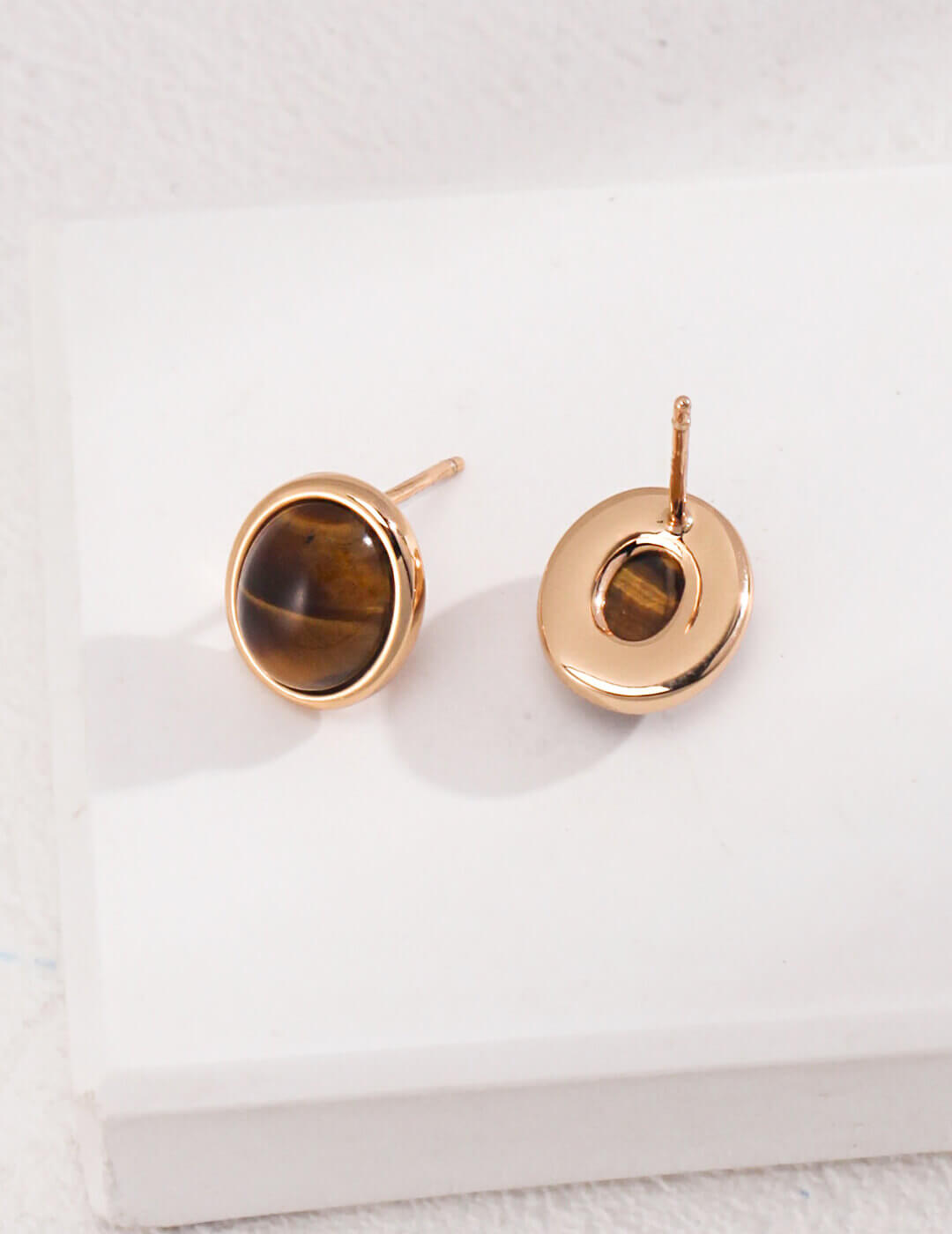 Gold earrings with tiger's eye stones on a white background