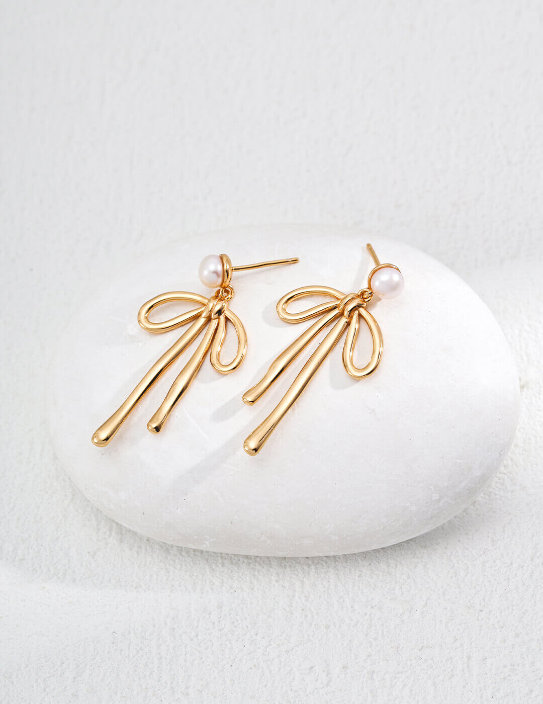 Gold earrings with pearl accents on a white stone surface