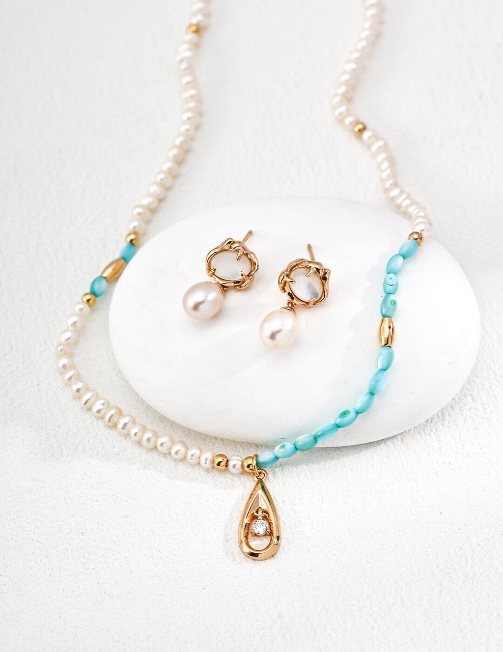 Pearl necklace with turquoise beads and gold accents on a white stone background