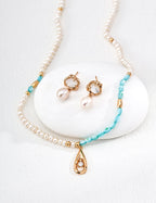 Pearl necklace with turquoise beads and gold accents on a white stone background