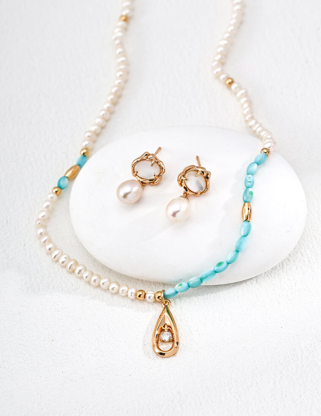Pearl necklace with turquoise beads and gold accents on a white stone background