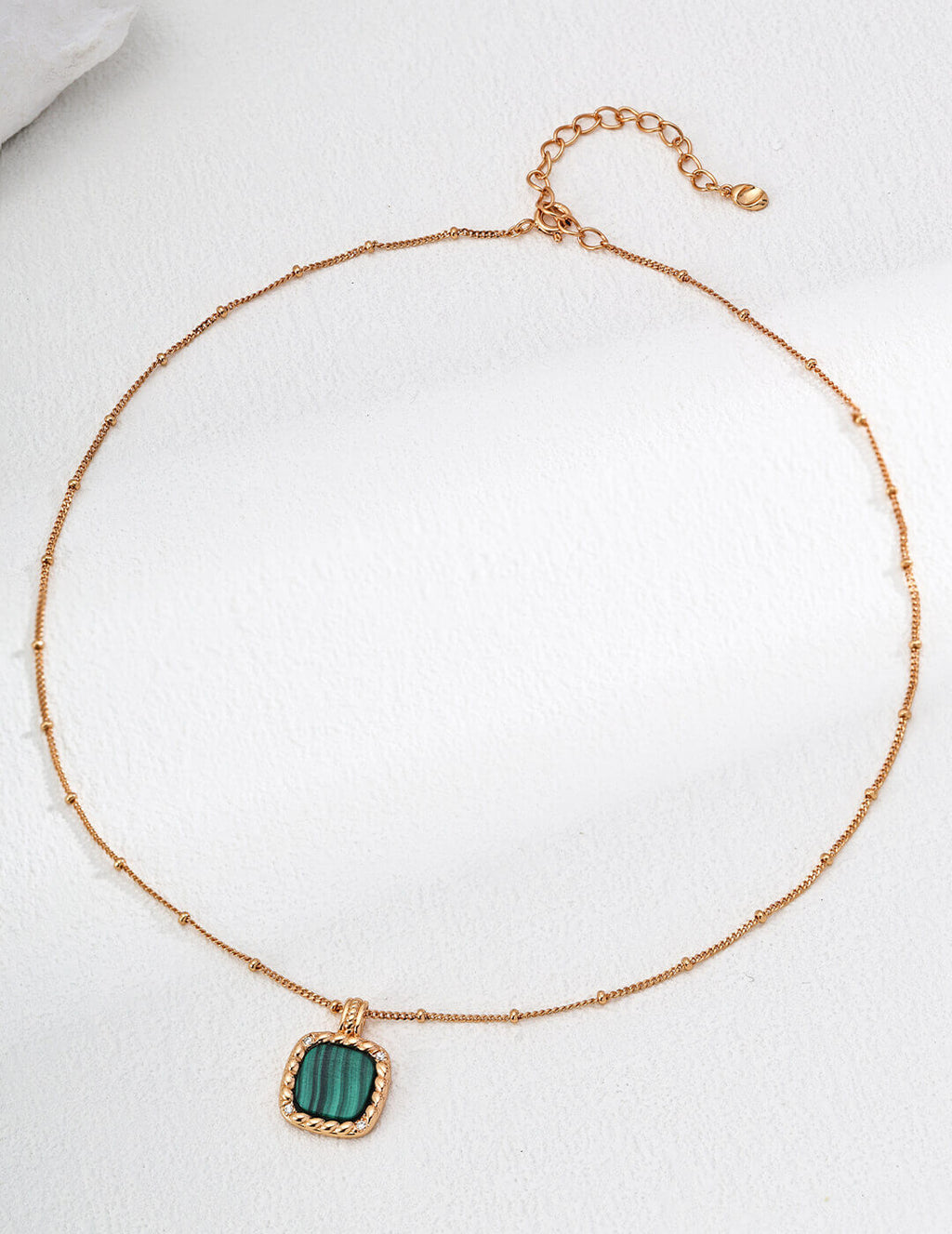 Gold necklace with a green pendant on a white background