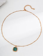Gold necklace with a green pendant on a white background