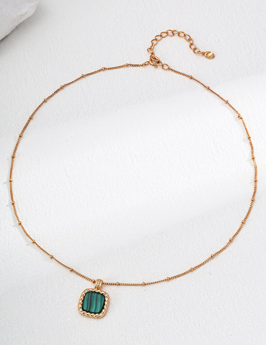 Gold necklace with a green pendant on a white background