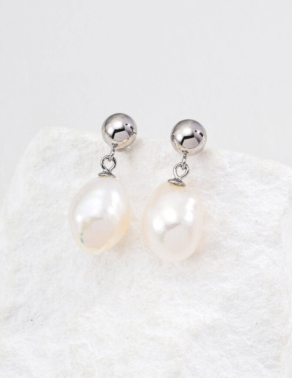 Pearl earrings with silver spherical tops on a textured white background