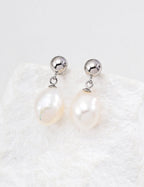 Pearl earrings with silver spherical tops on a textured white background