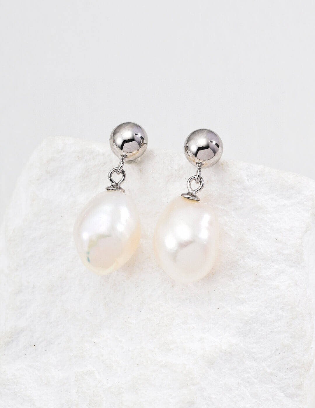 Pearl earrings with silver spherical tops on a textured white background