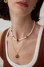 Close-up of a person wearing a pearl necklace and gold pendant necklace.