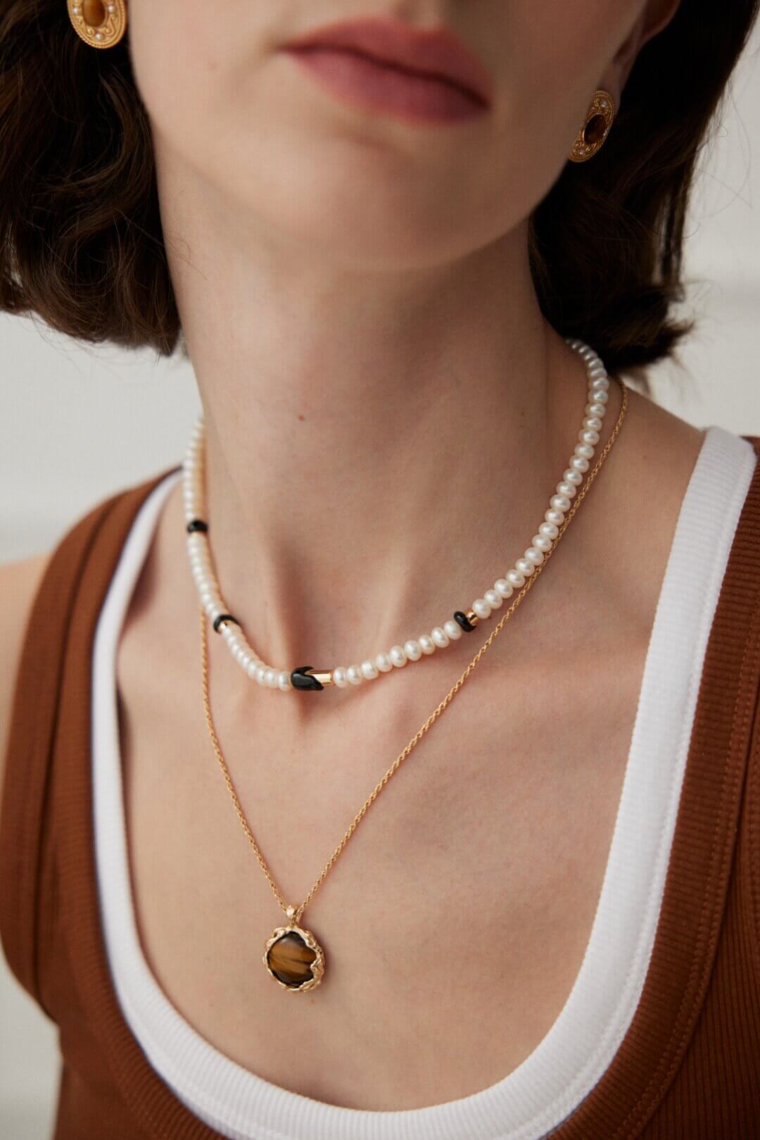 Close-up of a person wearing a pearl necklace and gold pendant necklace.
