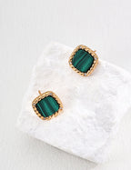 Gold earrings with green gemstones on a white fabric background