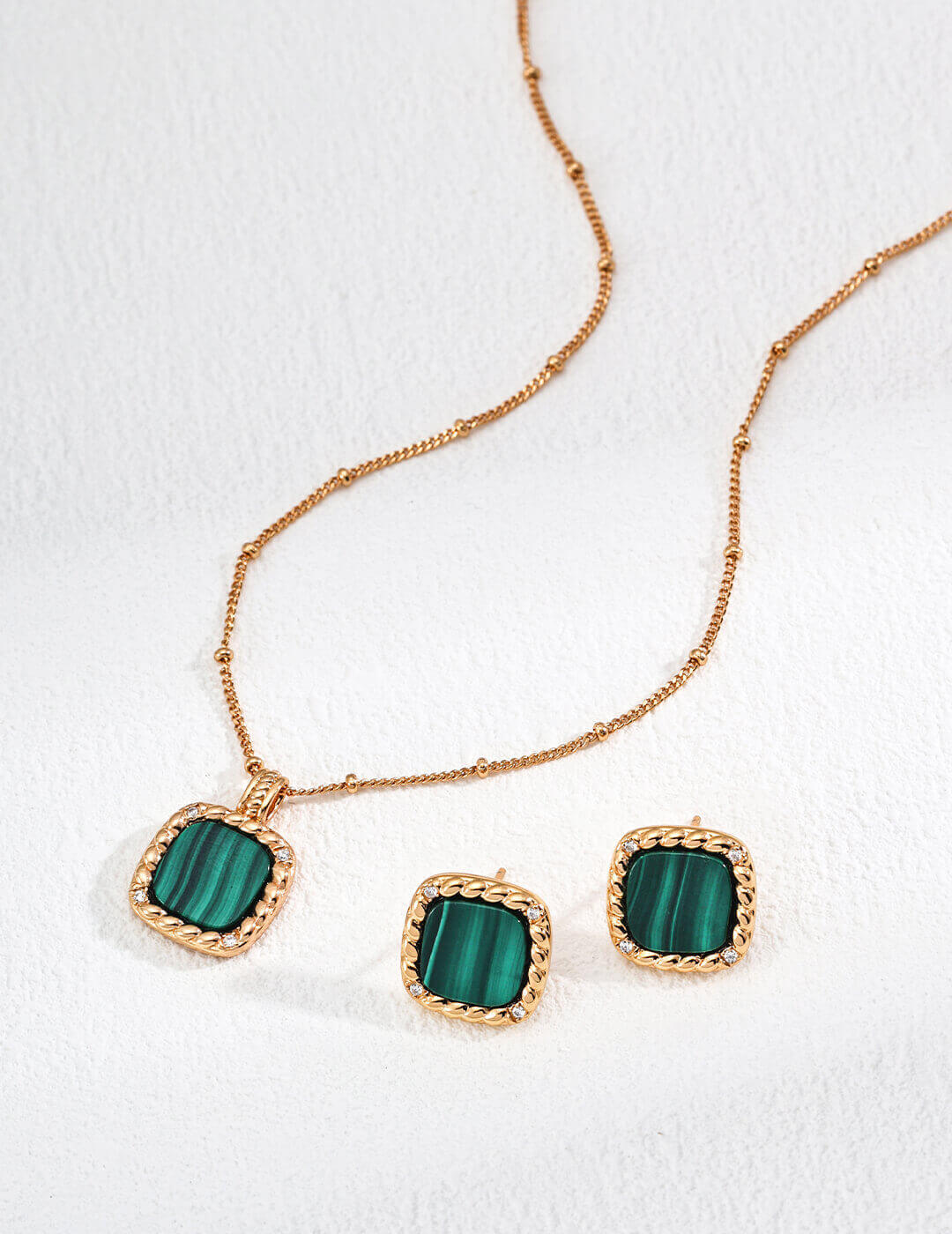 Jewelry set with green stones and gold accents on a white background